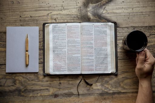 An overhead shot of a male holding his coffee mug near an open book on a wooden surface