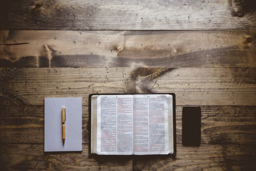 An overhead shot of an open book near a notebook and smartphone on a wooden surface