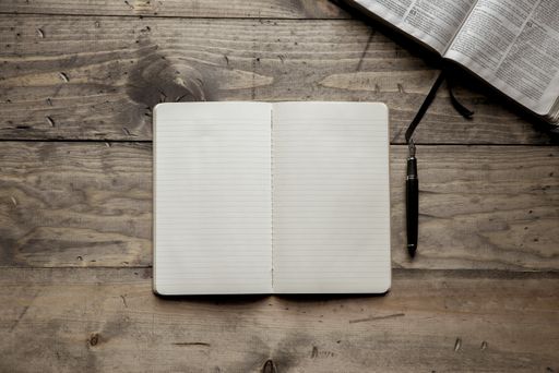An overhead shot of a blank notebook near a fountain pen on a wooden surface