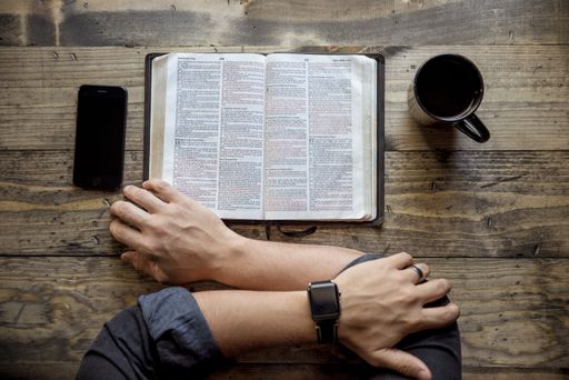 An overhead shot of a person reading a book near coffee and smartphone on the wooden table