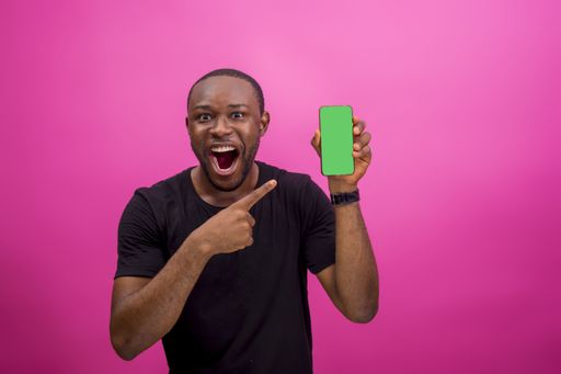 An African American male holding a cellphone while standing in front of a pink background