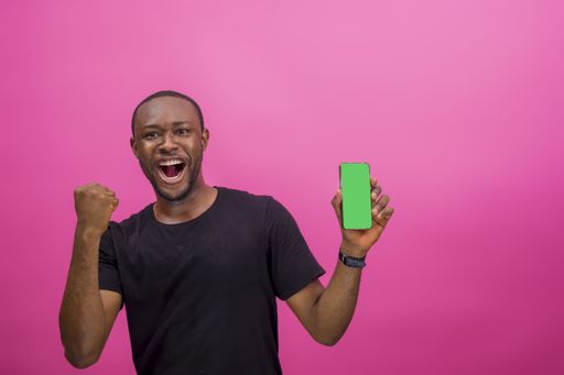 A young happy African american male using a smartphone isolated on a pink background