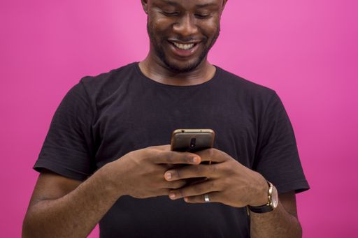 A young smiling black male looking at his smartphone screen