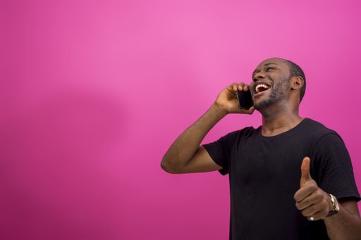 A young happy African american male using a smartphone isolated on a pink background