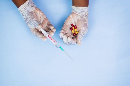 An overhead shot of a male in gloves holding pills and vaccine on a blue background