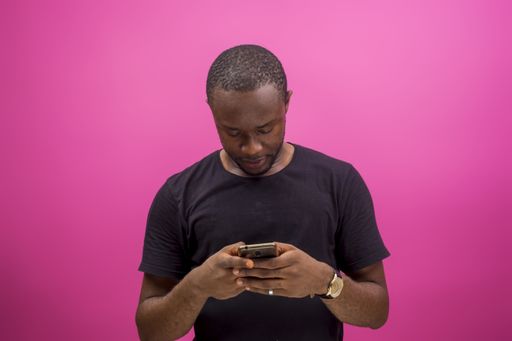 A young happy African american male using a smartphone isolated on a pink background