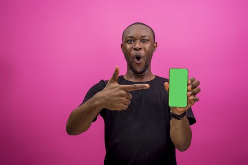 An African American male holding a cellphone while standing in front of a pink background