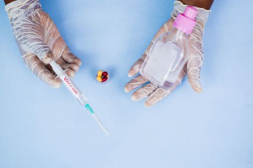 A high angle shot of a male hand wearing gloves and holding syringe and alcohol on a blue background