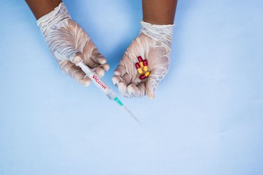 An overhead shot of a male in gloves holding pills and vaccine on a blue background