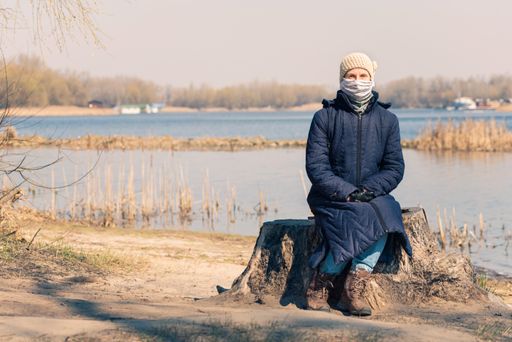 A poor elderly woman sitting on a tree and wearing a homemade mask to protect herself from the coronavirus