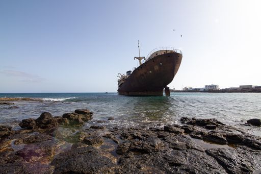 A low angle shot of an abandoned giant rusty ship near the seashore under the clear sky