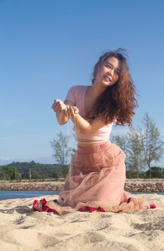 A vertical shot of a Vietnamese female wearing a light pink dress on a sandy beach