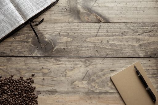 An overhead shot of a fountain pen on a notebook near book and coffee beans on a wooden surface