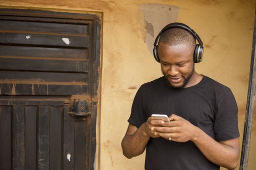 A happy African-American male wearing a headset while looking at the phone in-front of the door
