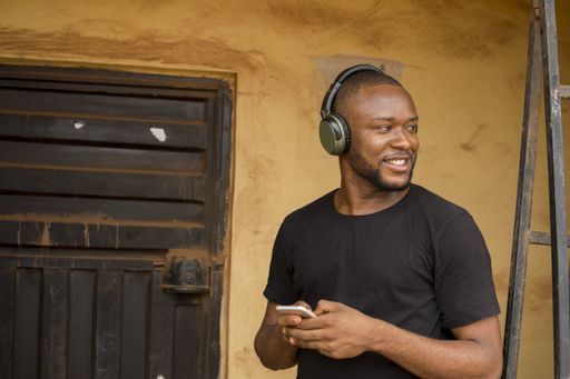 An African American male wearing a face mask and headset while using his cellphone