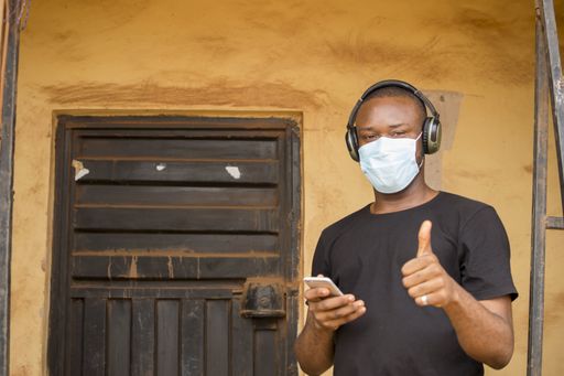 A happy African-American male wearing a mask and a headset while doing a thumbs up in front of the door