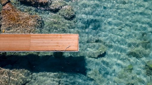 A top view shot of a wooden deck over the blue water