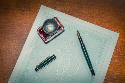 A high angle shot of a designed paper, a fountain pen and a jar of ink on a wooden surface