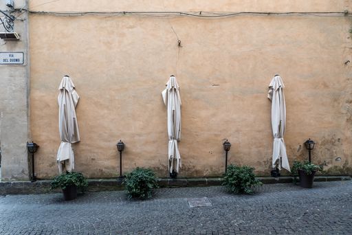 Table umbrellas next to an old wall and small green plants on the floor