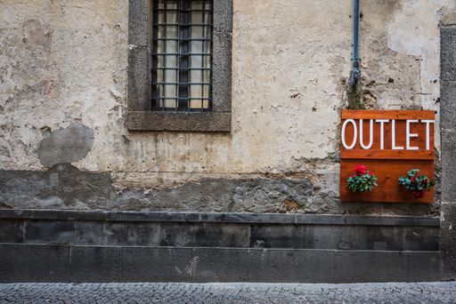 A closeup shot of an ancient wall with an old window and a wooden sign next to it with the "OUTLET" word