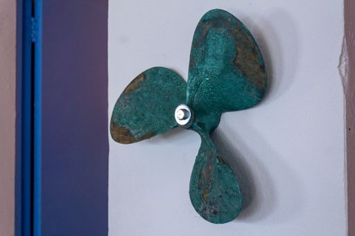 An old green rusty fan hanging from a white-colored wall with a blue door