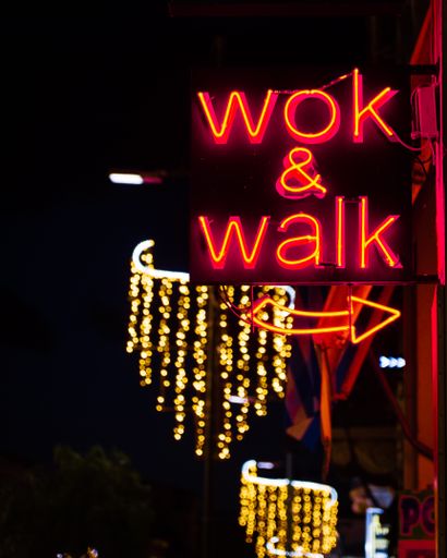 A vertical closeup shot of a neon advertisement reading "wok & walk" on an urban street