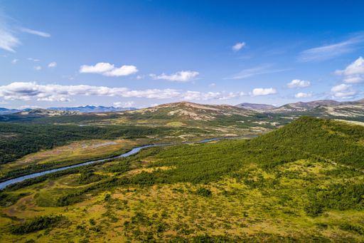 An aerial shot of mountains with a flowing river under a cloudy blue sky