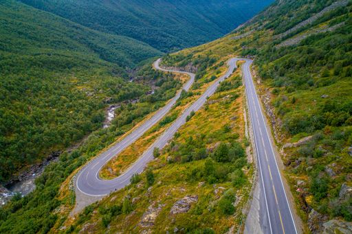 An aerial shot of an asphalt road on a green mountain near the river