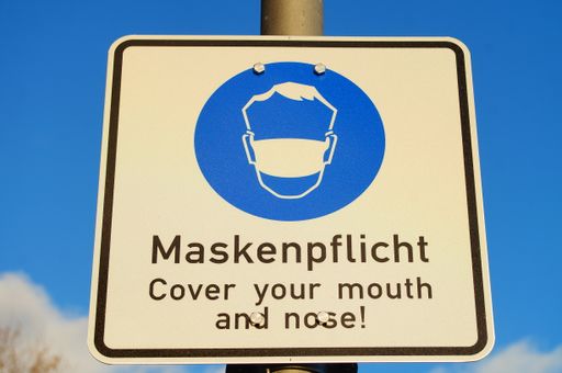 A sign indicates the obligation to wear a mask. Frankfurt, Germany, in Corona times. Blue sky with clouds. Nice blue in blue.