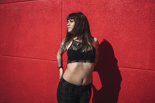 A young attractive Caucasian female with tattoos standing against a red wall