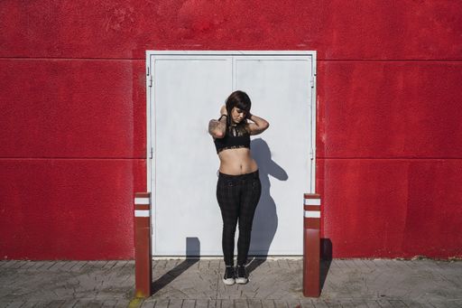 A young attractive Caucasian female with tattoos standing against a white iron gate and making a cute face