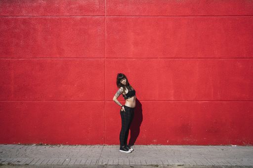 A young attractive Caucasian female with tattoos standing against a red wall