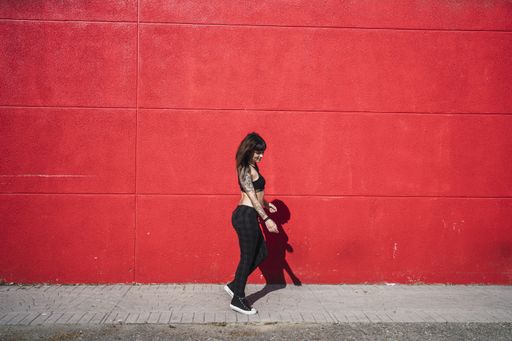 A young attractive Caucasian female with tattoos standing against a red wall