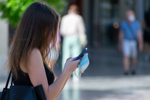 A shallow focus shot of a female texting on her phone with a medical mask in her hands