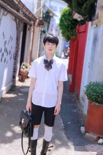 A shallow focus of a Korean male with shorts and a white shirt holding a bag under the sunlight