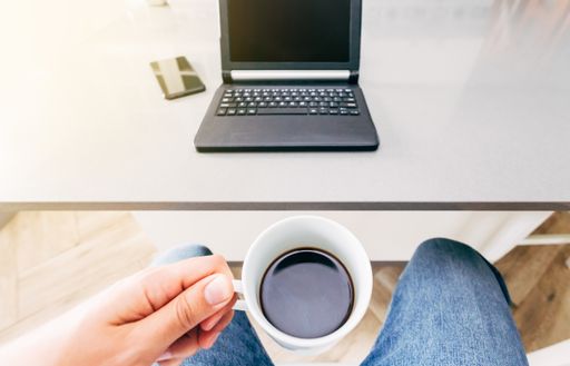 A high angle shot of a person drinking coffee while working on the computer