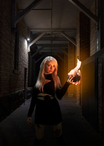 A portrait of a Caucasian female dressed in black holding a fireball in a dark room