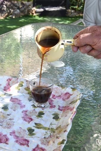 A vertical closeup of pouring traditional Druze black coffee from an old cezve into glass cups on the table