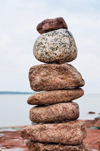 A vertical closeup shot of red stones stacked on top of each other against a body of water and a cloudless sky
