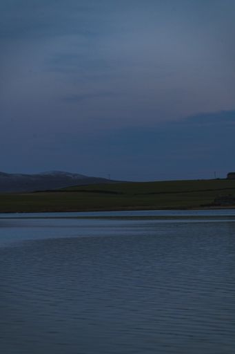 A vertical shot of a body of water near the sore with an evening sky in the background