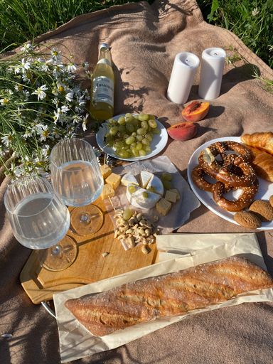 A vertical shot of food and drinks on a picnic blanket under a bright sunlight
