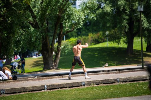 Strong athletic young man performs boxing exercises in a park. Workout during the summer in the Munich Olympic Park