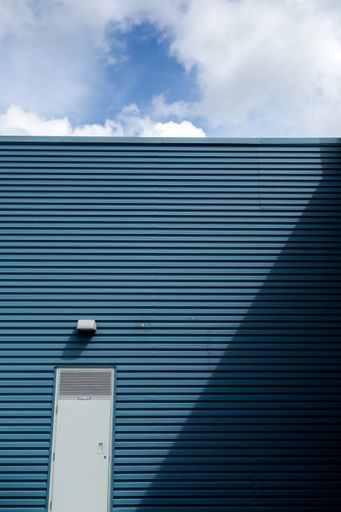 A vertical shot of the facade of a dark blue building with white door and lighting bulb on it against blue sky on a sunny day