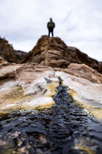 A low-angle vertical shot of rocks with a person standing on the edge of a cliff in the background