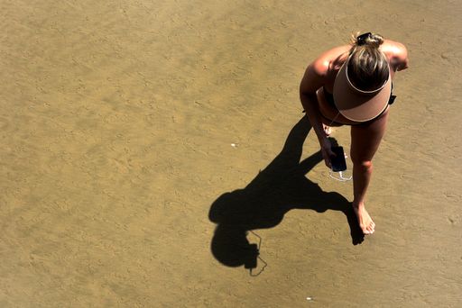 An overhead shot of a woman in a visor walking on a beach listening to music