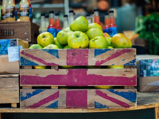 A closeup shot of a wooden fruit crate with the flag of UK drawn on it full of green apples