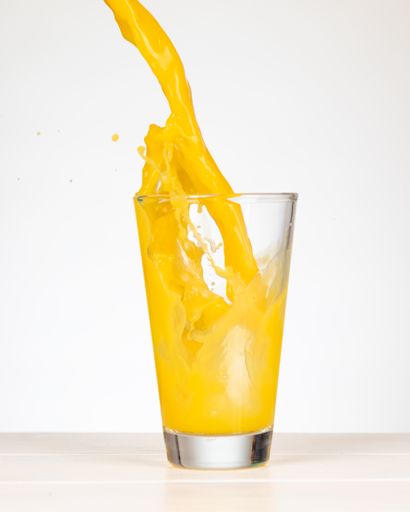 A vertical shot of pouring orange juice in a glass.