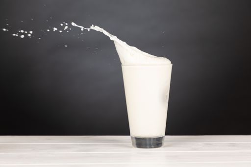 A  shot of milk in a glass with a splash in a black background.