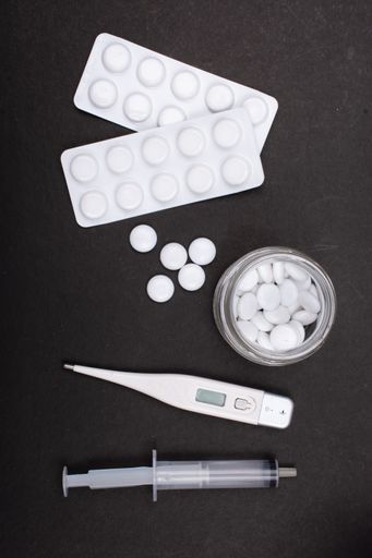 A vertical high angle shot of some pills, a thermometer, and a syringe on a black background