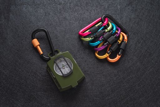 A top view of colorful carabiners and a green compass on black textured background